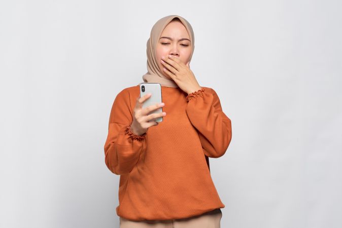 Muslim woman yawning while holding her smartphone