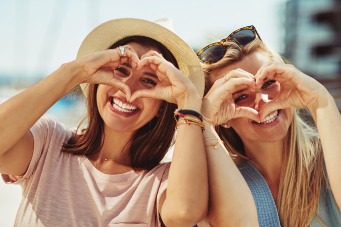 Women smiling and making hearts with their hands over their face