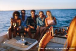 Close up of woman holding smart phone and taking picture of friends sitting on boat 5Q18V5