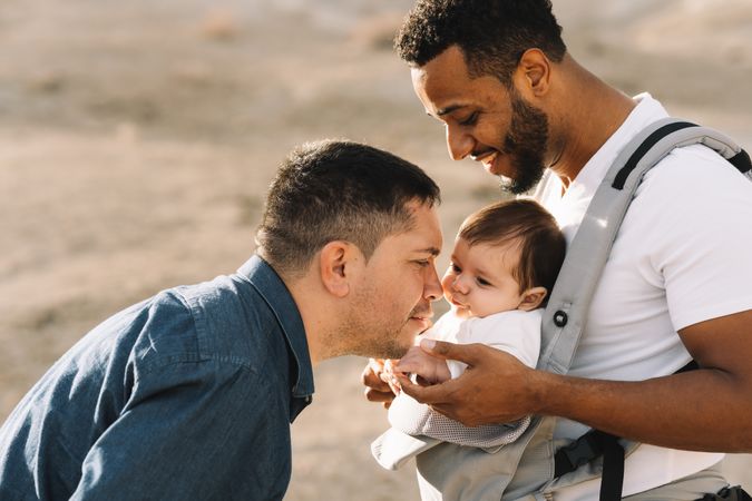 Unrecognizable diverse men walking with baby on nature