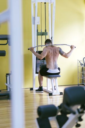 Tattooed male exercising his arms and back on pull down machine, vertical