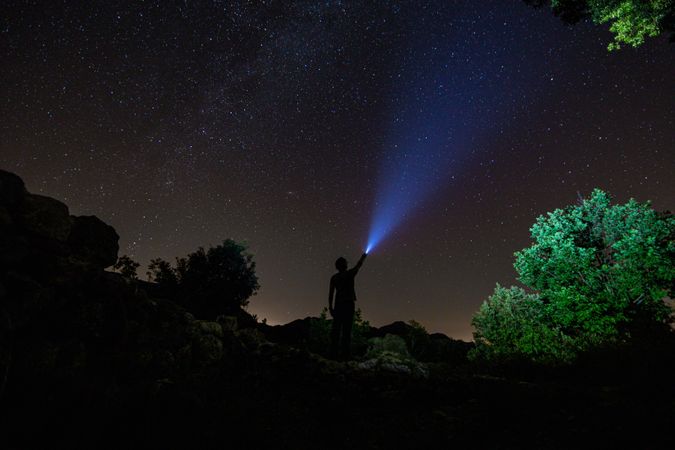 Person illuminating star with flashlight on hill