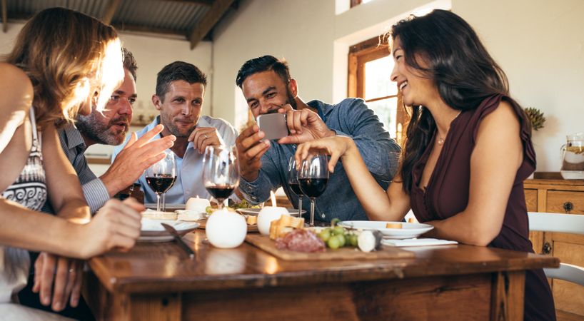 Group of men and women sitting around dinner table and looking at mobile phone