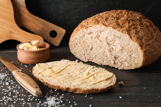 Cutting boards, bread, salt, knife and butter on wooden table against dark background, space for text