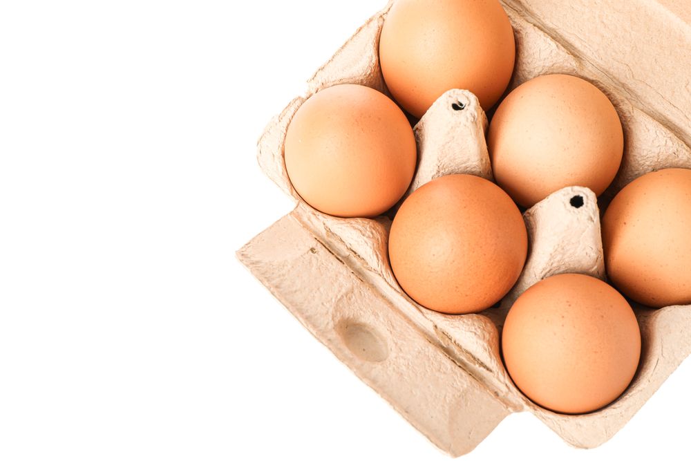 Brown chicken eggs in carton box isolated on light background, top view