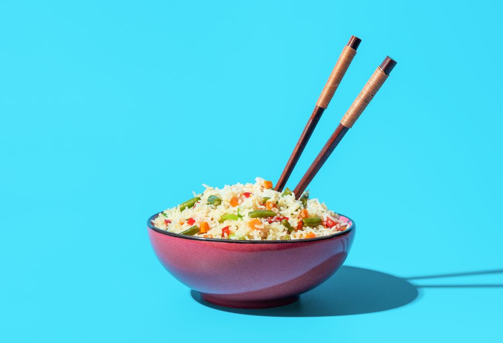 Bowl with fried rice and vegetables minimalist on a blue background