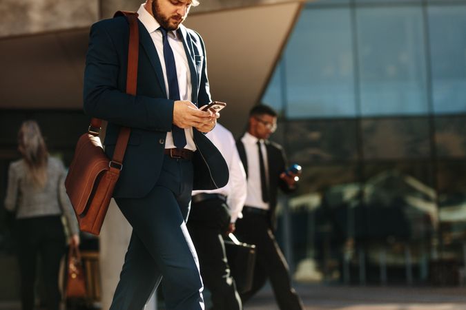 Business professional using mobile phone while walking on street to office