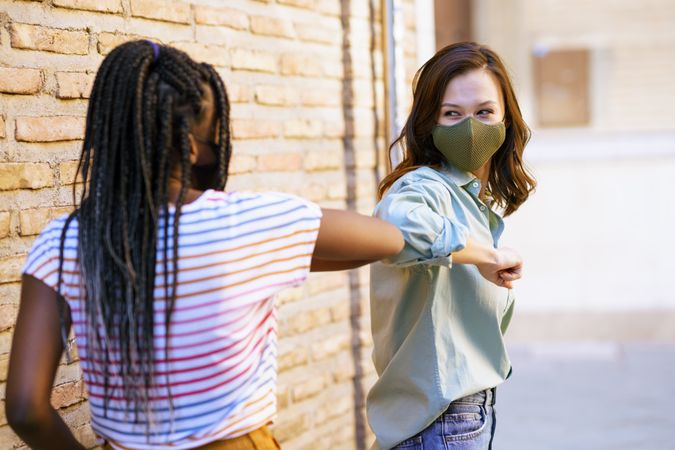 Female friends tapping elbows in lieu of shaking hands protecting themselves from virus