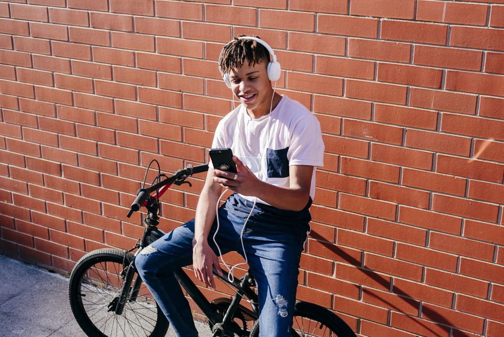 Young happy Black male listening music with smartphone on bike