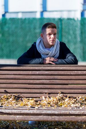 Teenage male sitting behind a wooden bench in a city park