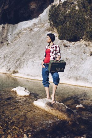 woman standing on rock with case near clear water in lake