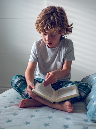 Little preschool boy sitting on bed and flipping through book