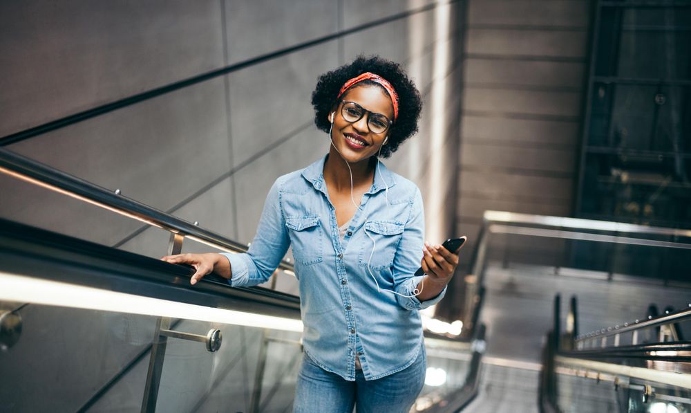 Woman smiling at camera while holding a phone on an escalator