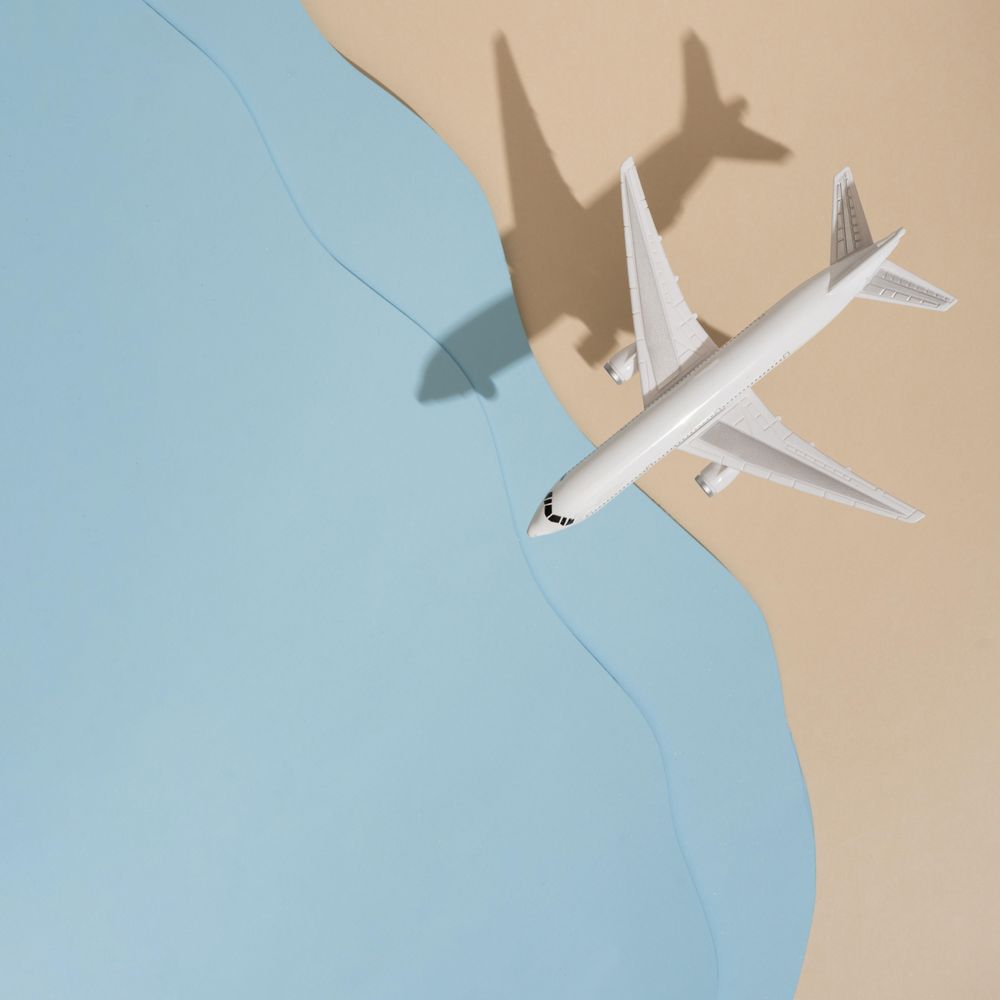 Top view of model airplane with shadow over beige and blue water beach scene
