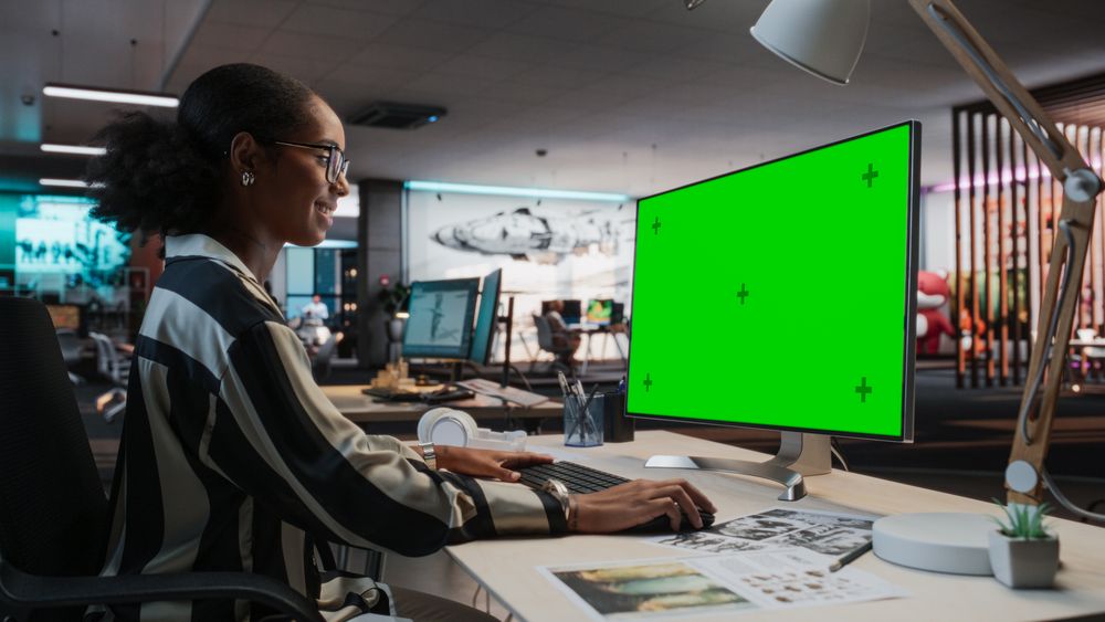 Portrait of Creative Black Female Sitting at a Desk Using Desktop Computer with Mock-up Green Screen.