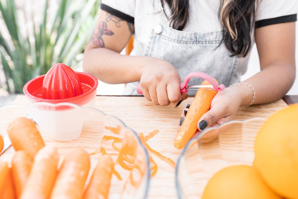 A young Hispanic woman is peeling some carrots to make orange and carrot juice outdoors