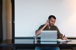 Cheerful man talking on smartphone near laptop
