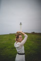 Woman walking in green meadow near lighthouse