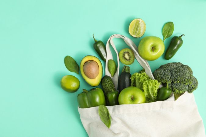 Bag with vegetables and fruits on mint background
