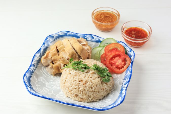 Hainanese Chicken Rice with Garlic and Chilli Oil on Wooden Table Background.