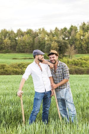Two laughing men in plaid shirt standing in long grass with forest in background