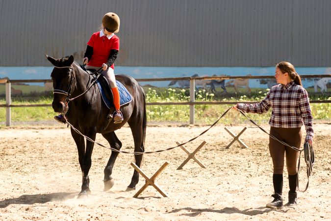 Young rider practices horseback skills with instructor's guidance.