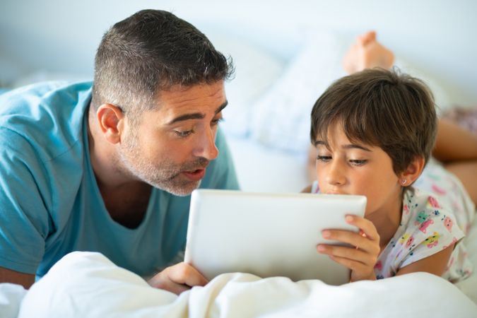 Father with child watching something on tablet in bed