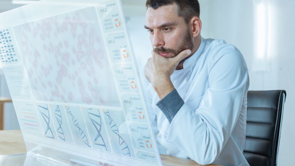 In the Futuristic Laboratory Male Scientist Works on Deciphering DNA Sequence on His Transparent Computer Display.