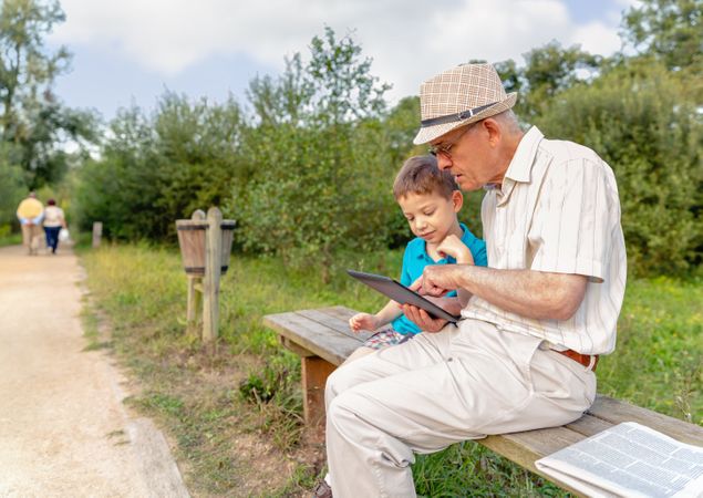 Grandchild with grandfather, using a tablet outdoors