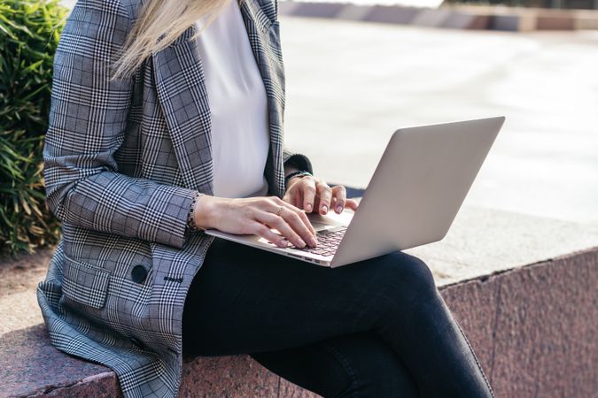 Unrecognizable business woman in suit working with laptop outdoors