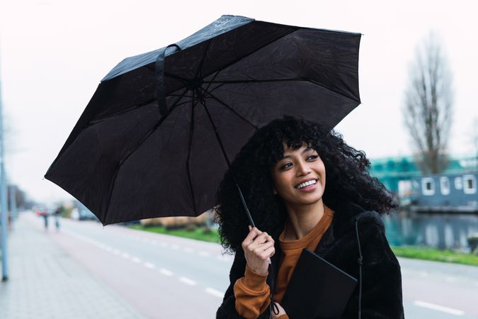 Smiling Black woman with umbrella on street