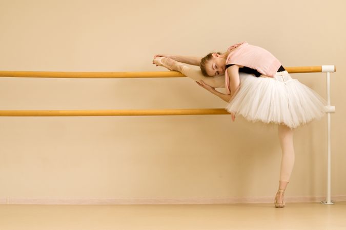 Ballet dancer stretches by placing her leg on barre
