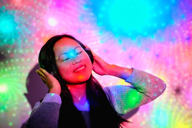 Delighted Asian woman listening to music under colorful lights