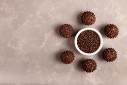 Top view of chocolate truffles arranged around bowl of sprinkles on marble surface with space for text