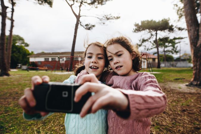 Little girls taking selfie using old camera at the park