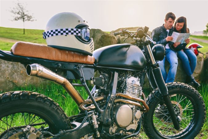 Custom motorcycle with helmet and young couple looking at a map