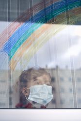 Boy with face mask standing near window with reflection of rainb