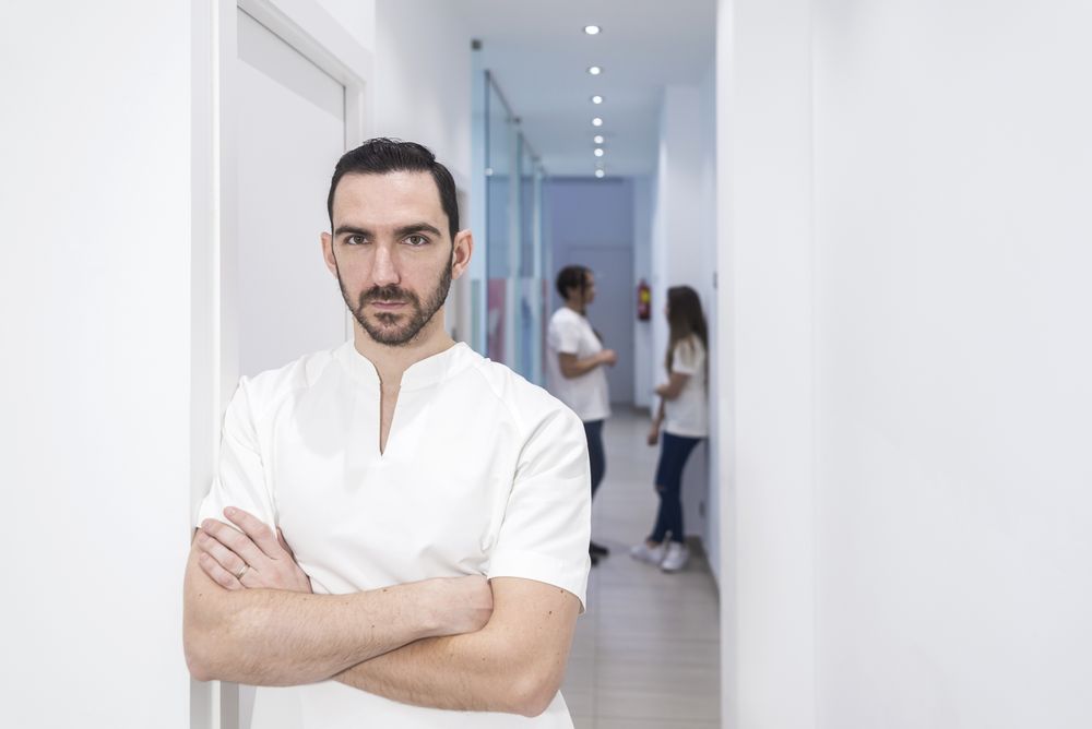 Portrait of a bearded male doctor standing with arms crossed in hallway