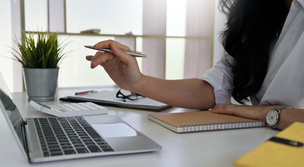 Woman holding a pen in hand pointing to a laptop screen