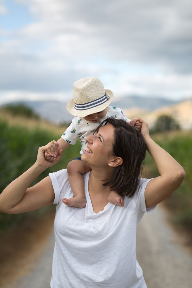 Adorable kid in hat on shoulders and looking at mother