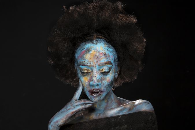Woman with afro hair and blue paint closing her eyes