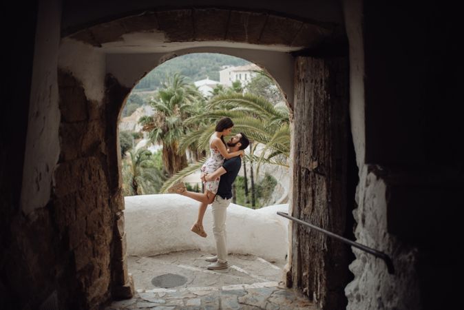 Affectionate couple embracing while standing on street in old arch of tropical town