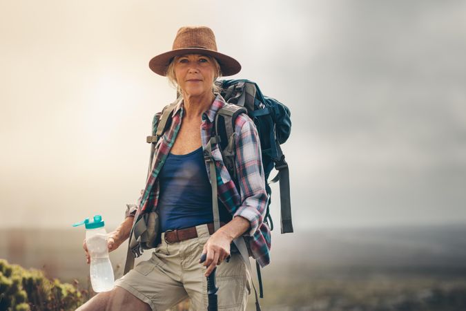 Portrait of a mature woman on a hiking trail drinking water standing on a hill