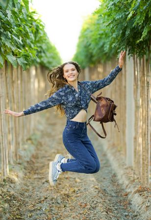 A Joyful Young Woman Jumping Enthusiastically in a Beautiful Vineyard with a Backpack on