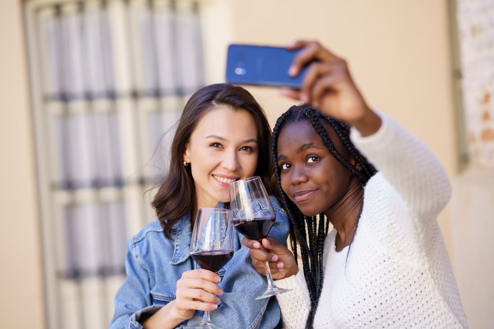 Female friends at an outdoor restaurant with red wine taking a self portrait