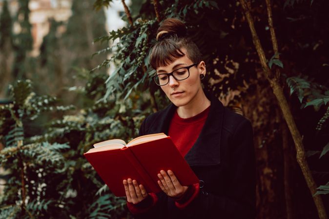 Young woman reading book on bench in park