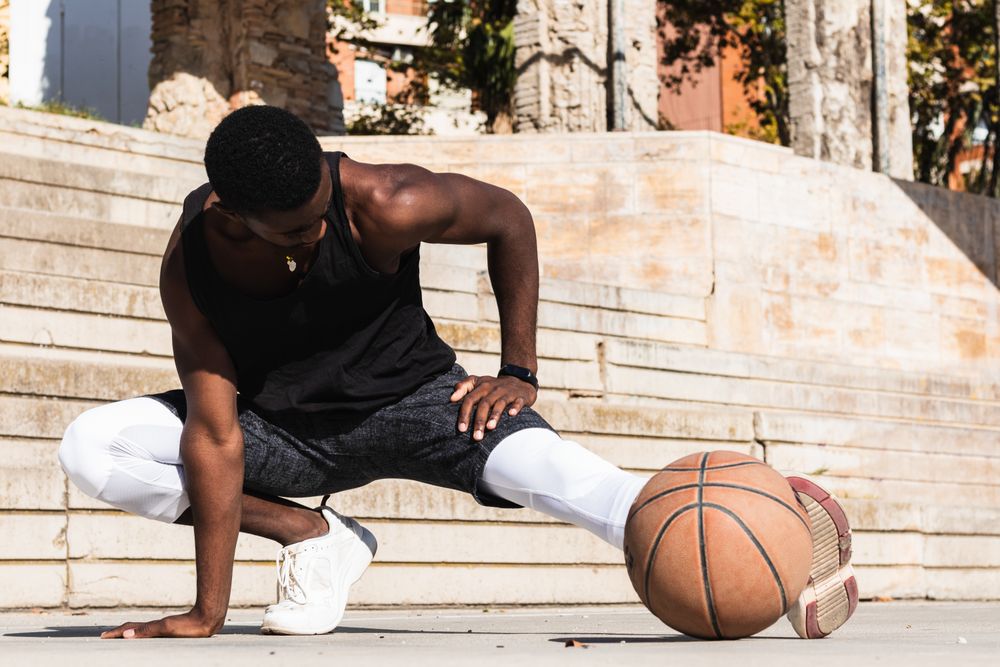 Black sportsman stretching on basketball court