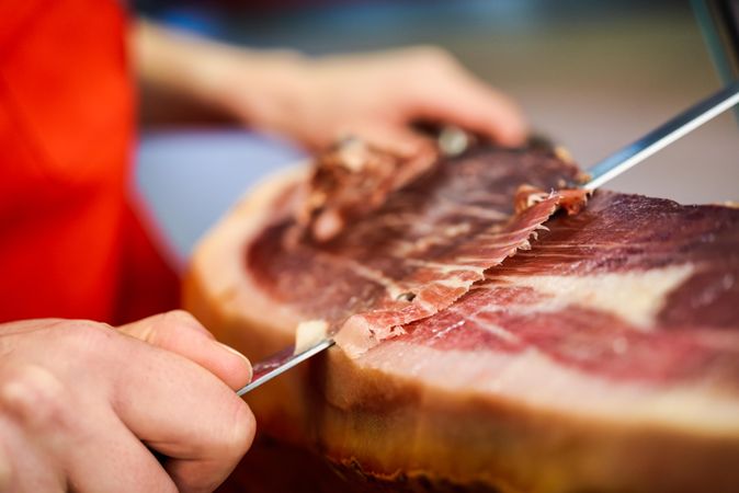 Close up of woman’s hands in butcher shop slicing meat