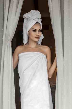Woman in bathing towels standing by window
