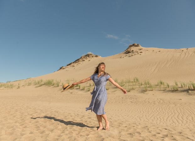 adult woman in casual dress and straw hat running having good time on sand dune